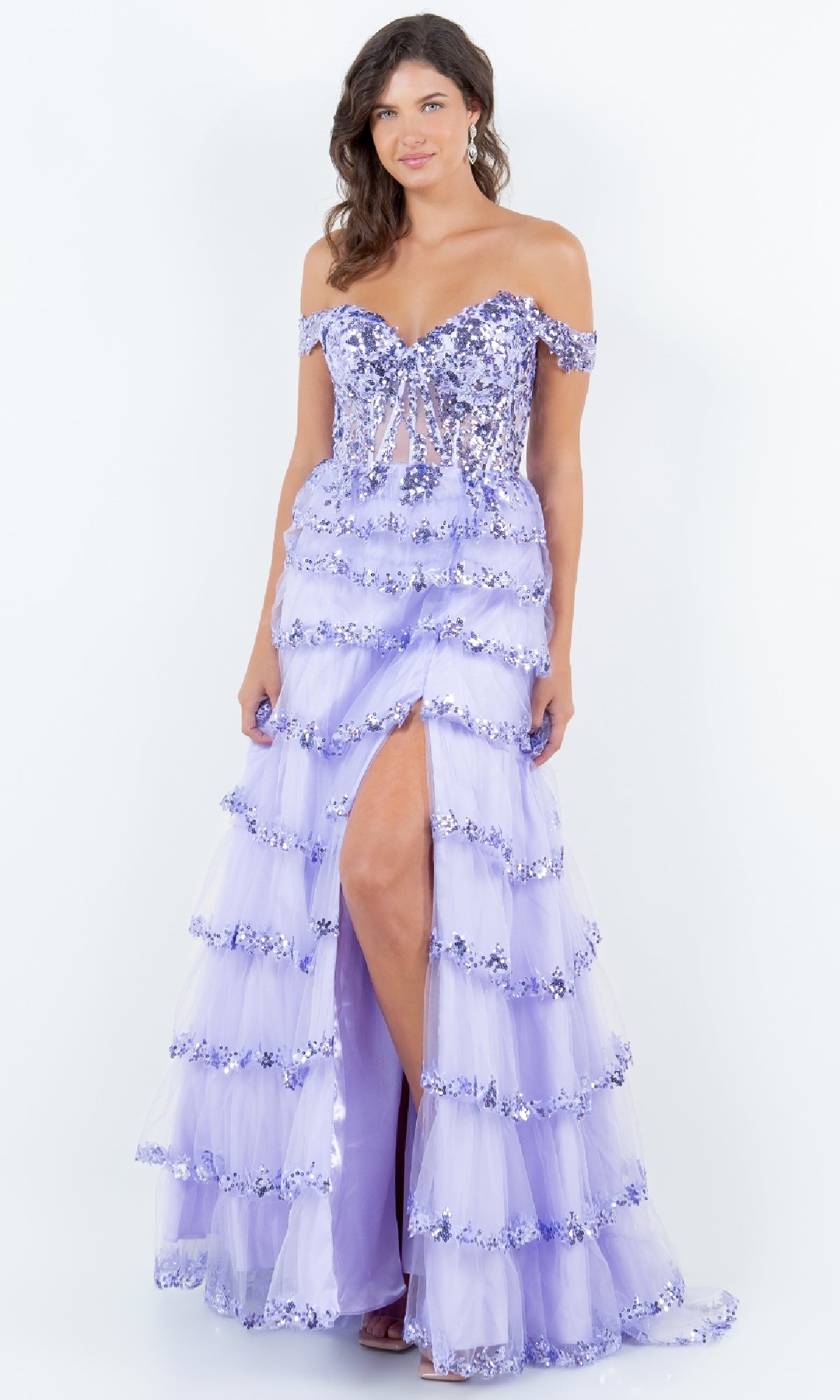 A woman wearing the Cinderella Couture 8228J Ruffle Prom Ball Gown in lilac, featuring off-the-shoulder sequin embroidery, layered tulle, and a thigh-high slit, stands against a plain white background.
